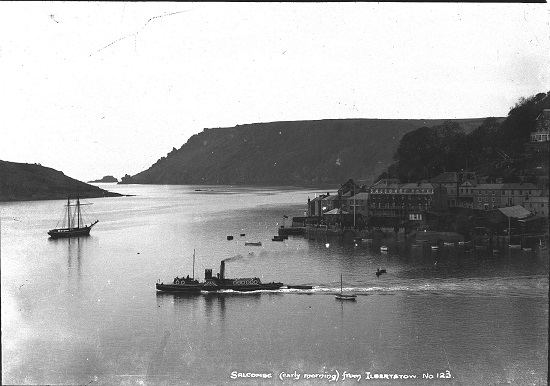 Salcombe (early morning) from Ilbertstow. 1900 = 1920. Paddle steamer - either  'Ilton' or  'Salcombe Castle' under way in foreground, two-masted vessel moored in midstream. Town shows ferry landing, Salcombe Hotel (before extension), Fore Street houses and boatyard (Fairweather Collection).